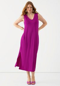 Fuchsia mouwloze maxijurk met een V-halslijn, voorzien van een zijsplit en een gladde textuur. Gecombineerd met bijpassende sandalen met hoge hakken.