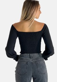 Top nero a maniche lunghe con schiena smock e scollatura quadrata ampia; abbinato a jeans in denim grigi a vita alta con tasche posteriori.