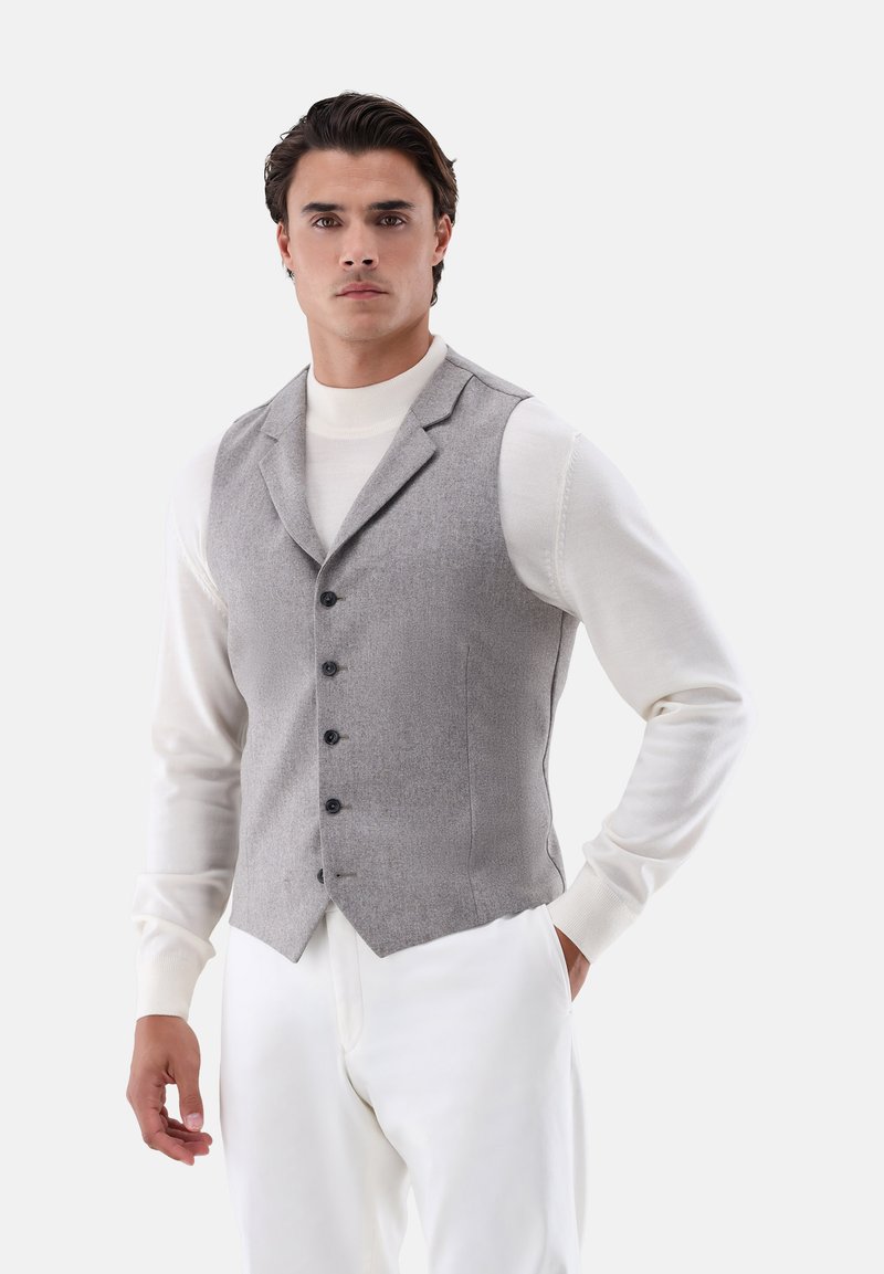 Grau wollene Weste mit taillierter Passform, fünf Knöpfen und scharfem Revers, getragen über einem weißen Rollkragenpullover und kombiniert mit weißen Hosen.