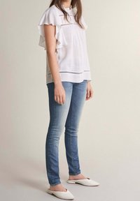 Top blanc à manches volantées et broderie horizontale, associé à un jean slim bleu clair et des mules blanches à enfiler.