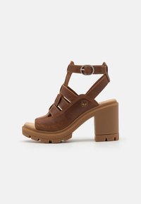 Brune læder hæle sandaler med åben tå, der har flere stropper og en justerbar ankelspænde. Chunky, tekstureret hældesign.