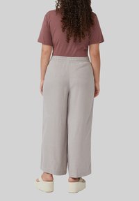 Lichtgrijze wijde broek met een elastische tailleband, gecombineerd met een mauve shirt met korte mouwen en beige platte sandalen.