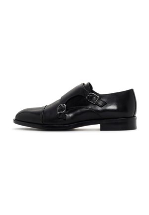 Scarpa formale in pelle nera con doppia fibbia monk strap, tacco basso e punta arrotondata, esposta su uno sfondo bianco.