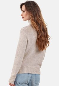 Pull beige clair à col roulé avec un tricot texturé, poignets et ourlet côtelés, porté avec un jean en denim bleu, vu de dos.