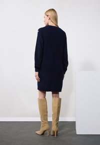 Abito in maglia blu navy con maniche lunghe, texture a coste e scollatura rotonda. Abbinato a stivali beige al ginocchio con tacco, in materiale scamosciato.