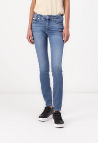 Smal denimjeans i ljusblått med medelhög midja, fem fickor och subtila sömnadsdetaljer, matchade med svarta sneakers.