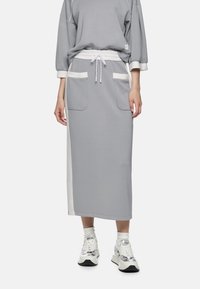 Grauer Rock mit Kordelzug in der Taille, zwei Fronttaschen und weißen Seiteneinsätzen. Kombiniert mit strukturierten Sneakers. Glatter Stoff, entspannte Passform.
