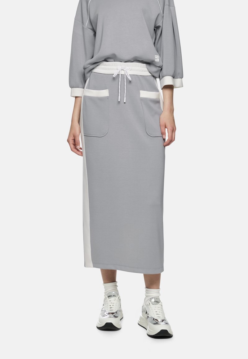 Grauer Rock mit Kordelzug in der Taille, zwei Fronttaschen und weißen Seiteneinsätzen. Kombiniert mit strukturierten Sneakers. Glatter Stoff, entspannte Passform.