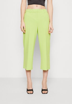 Zielone limonkowe szerokie spodnie o skróconej długości, noszone z czarnymi szpilkami z odkrytymi palcami i czarnym krótkim topem, pokazane na jednolitym jasnym tle.