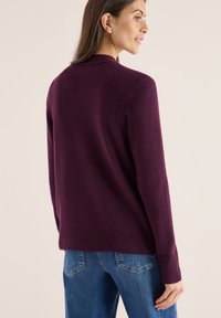 Maglione a maglia di un profondo viola, con scollatura rotonda e polsini a costine. La vista posteriore mostra una texture liscia e una vestibilità rilassata. Abbinate a jeans blu.