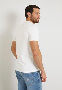 Valge lühikeste varrukatega t-särk, slim fit, ühtlane kaelus, kantud helesiniste denimpükstega, millel on tagataskud ja logo detail.