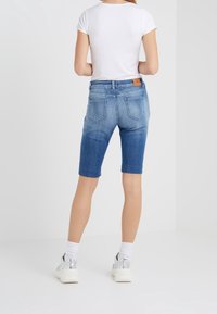 Tummansinisiä denim-bermuda-housuja, joissa on viisi taskua ja ruskea nahkasteri vyötäröllä. Yhdistettynä valkoisiin tennareihin.