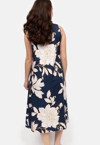 Granatowa sukienka bez rękawów z dużymi białymi wzorami kwiatowymi z pomarańczowymi akcentami, do kolan, gładki materiał o luźnym kroju.