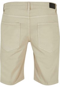 Pantalones cortos de algodón beige con un corte recto, dos bolsillos traseros y una etiqueta en la cinturilla de color negro. Diseño limpio y detalles de costura robustos.