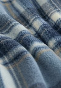 Fleece-Decke in Blau-, Creme- und Hellbrauntönen, mit einem Karomuster und weicher Textur, die durch Wellen im Stoff Tiefe erzeugt.