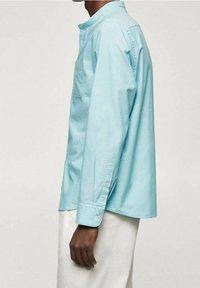 Hellblaues Hemd aus Baumwolle mit Knöpfen, ausgestattet mit einem Kragen, langen Ärmeln und einer Brusttasche. Der Schnitt ist locker mit einem längeren Rückensaum.