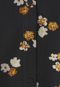 Tecido preto texturizado com bordado floral em amarelo, laranja e branco. Apresenta botões pretos ao longo da frente.