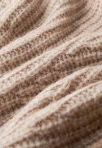 Tela de punto de color marrón claro con textura acanalada, que presenta fibras suaves y esponjosas que crean una apariencia cálida y acogedora.