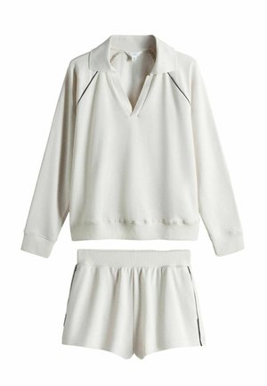 Kremfarvet langærmet pullover med krave og matchende elastiske shorts, begge med tynd sort piping langs kanterne.