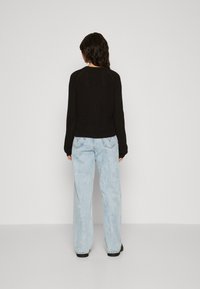 Zwarte gebreide trui met lange mouwen, gecombineerd met lichtblauwe wijde jeans. De trui heeft een gestructureerde afwerking en een geribde zoom.