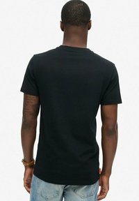 Camiseta negra de manga corta exhibida desde la parte de atrás, con un corte clásico y material de algodón suave, sin patrones ni logotipos visibles.