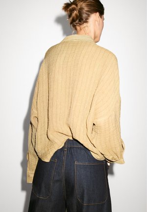 Lös passform, texturerad senapsgul skjorta med krage, långa ärmar och sänkt axel, kombinerad med mörka denimbyxor med stora bakfickor.