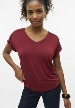 Bordeaux v-hals t-shirt med korte, rullede ærmer, lavet af blødt stof. Båret med mørke jeans og et kraftigt armbånd på håndleddet.