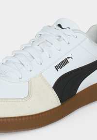 Λευκό αθλητικό παπούτσι Puma με μαύρη ρίγα, καφέ σόλα, λευκά κορδόνια και λογότυπο Puma στο πλάι και στη γλώσσα.
