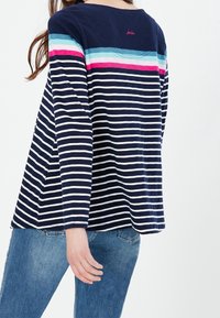 Marineblauwe langharige shirt met horizontale witte strepen, met een kleurrijk gestreept paneel over de schouders in roze en turquoise.