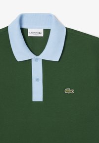 Grön polotröja med ljusblå krage, tvåknapps knäppning och broderad krokodil-logotyp. Strukturerad tyg med en klassisk passform.