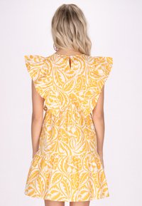 Rochie galbenă cu model de frunze albe, cu mâneci evazate și fustă stratificată. Include un închizător cu buton la spate. Confecționată dintr-un material ușor.