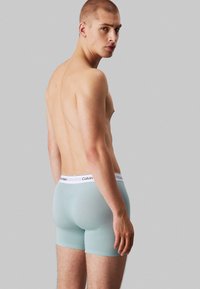 Lichtblauwe boxershort van zacht materiaal, met een witte elastische band met "Calvin Klein" branding. De achterkant toont een aansluitende pasvorm en een subtiele textuur.