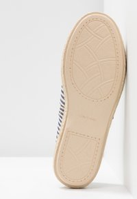 Semelle d’une espadrille beige avec un motif antidérapant texturé et la mention « Made in Spain », montrant partiellement la tige en tissu rayé bleu et blanc.
