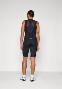 Svarte sykkel-bibshorts med mesh-top og polstret sete. Har et tettsittende design og reflekterende detaljer. Glatt, elastisk stoff gjennom hele.