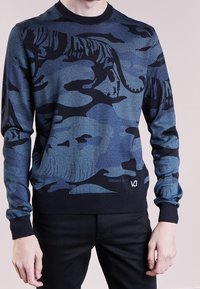 Pull en camouflage bleu présentant un motif de tigre, avec un col rond et des poignets côtelés, et un logo au bas. Fabriqué en tissu doux et texturé.