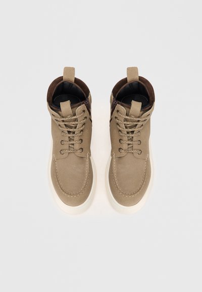 Botas de tobillo de ante beige con acentos marrones, punta redonda, diseño con cordones y suela de goma blanca. Cuello texturizado para mayor detalle.