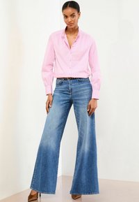 Cămașă button-up cu dungi roz deschis, cu corp ajustat și mâneci strânse, asociată cu blugi evazați din denim albastru și pantofi cu toc înalt, maro.