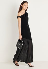 Czarna welurowa sukienka na jedno ramię z lejącym się, przejrzystym dołem, w zestawieniu z torebką w groszki i czarnymi szpilkami na paski. Gładka faktura, elegancki design.