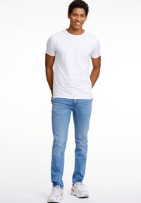 White cotton t-shirt, short sleeves, paired with light blue denim jeans and white sneakers featuring gray accents and orange detail.