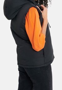 Black puffer vest with a hood, featuring a smooth texture, worn over an orange long-sleeve shirt. The vest has side pockets and a zipper.
