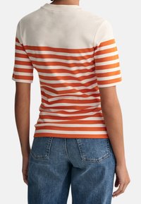 Camiseta de manga corta a rayas con líneas horizontales en naranja y blanco, cuello redondo y tejido suave. Combinada con unos vaqueros de mezclilla azul.