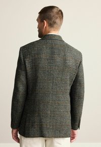 Gråternet blazer med en struktureret overflade, med slidser bagpå og reverskrave. Den har forskellige farver, herunder brun og grøn.