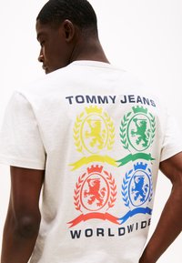 Lys grå bomulls t-skjorte med rund hals. Har et fargerikt grafisk design av løver i sirkulære mønstre og tekst med "TOMMY JEANS WORLDWIDE".