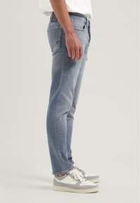 Vaqueros de mezclilla azul claro con corte ajustado, que presentan costuras mínimas y una textura suave. Acompañados de zapatillas gris y blancas.