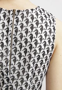 Vitt tyg med ett upprepande mönster av svarta sjöhästar. Har en metallisk dragkedja baktill, med en mjuk och lätt textur.