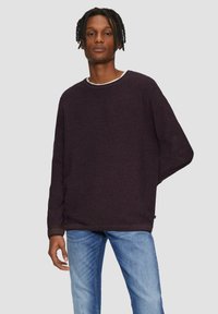 Dunkelviolettes Langarm-Sweatshirt mit Rundhalsausschnitt, strukturiertem Stoff und gerippten Bündchen, kombiniert mit hellblauen Jeans.