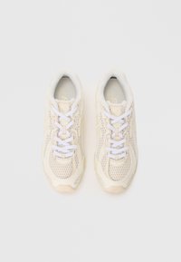 Baskets beige clair avec un dessus en mesh, lacets blancs et embout renforcé. Semelle texturée et détail de logo subtil sur la languette.