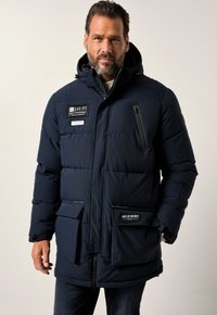 Marineblauer Puffermantel mit Kapuze, ausgestattet mit Reißverschlusstaschen und Logo-Patches. Der Stoff wirkt strukturiert und das Design ist warm und isoliert.