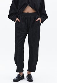 Svarta denimbyxor med avslappnad passform, elastisk midja, sidofickor och ett subtilt vertikalt randmönster. Matchas med svarta loafers.