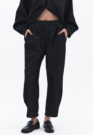 Zwarte denim broek met een relaxed fit, elastische tailleband, zijzakken en een subtiel verticaal streepjespatroon. Gekleed met zwarte instappers.